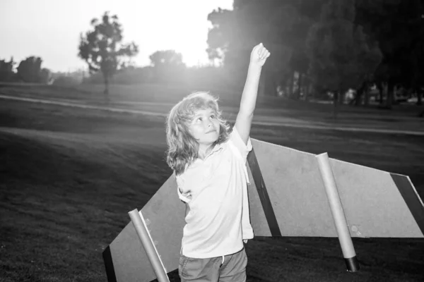 Leader et vainqueur des enfants, démarrage réussi. Enfant excité garçon jouer avec jouet jetpack ailes super-héros dans le parc au coucher du soleil. — Photo