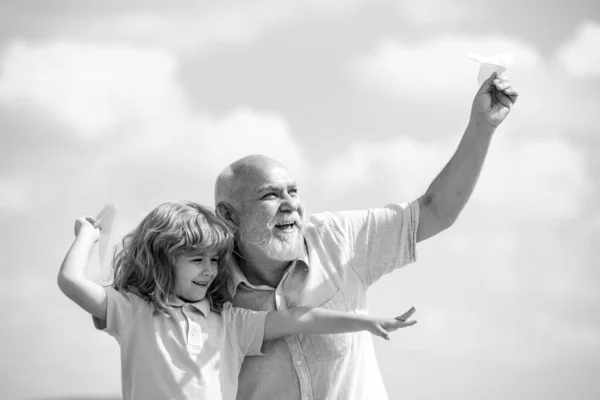 Mavi gökyüzü ve bulutların üzerinde kağıt uçakla uçan çocuk ve büyükbaba. Erkek nesli büyükbaba ve torun. Yaşlı bir akraba ve çocuk.. — Stok fotoğraf