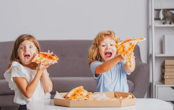 Niños comiendo pizza. Niños emocionados comiendo pizza. Dos niños pequeños muerden pizza adentro. — Foto de Stock