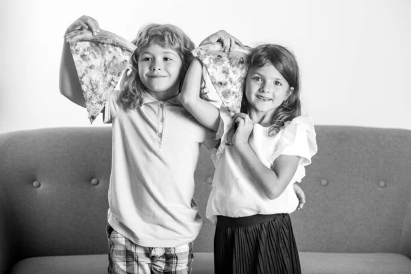 Filha feliz e filho comendo pizza. Crianças crianças desfrutar e se divertir com o almoço juntos em casa. Crianças engraçadas comendo pizza e se divertindo juntas, segurando uma fatia de pizza perto do rosto. — Fotografia de Stock