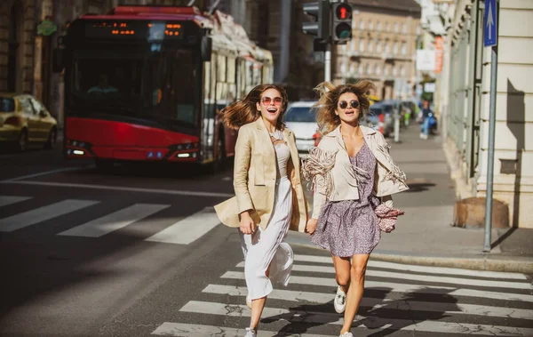 Kilépett barátok lányok futás a zebrán, nagy időt töltenek együtt a nyári utcában város. — Stock Fotó