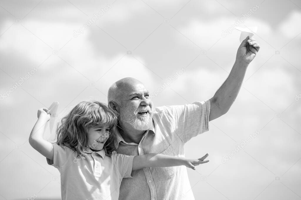Child boy and grandfather with paper plane over blue sky and clouds. Men generation granddad and grandchild. Elderly old relative with child.