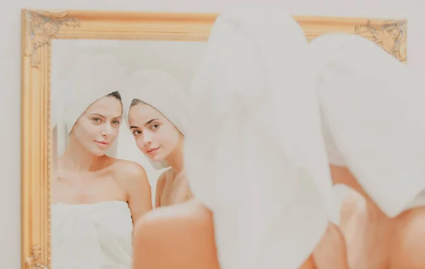Primer plano hermosa mujer mira en el espejo después de la ducha. Jovencitas amigas guapas envueltas en toalla alisando la piel perfeccionando, concepto de rutina diaria matutina. —  Fotos de Stock