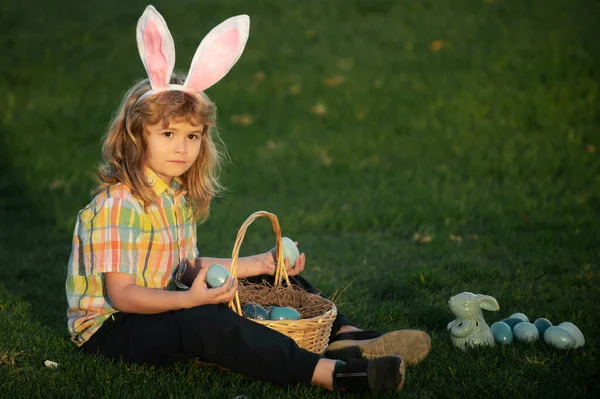 Des lapins avec des oreilles de lapin. Enfant garçon chasse oeufs de Pâques dans la pelouse de printemps ponte sur l'herbe. — Photo