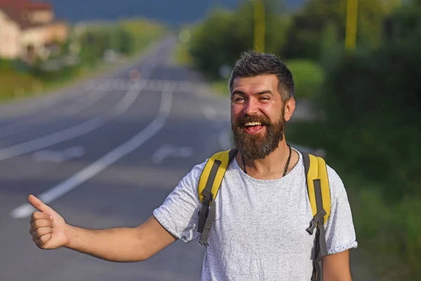 Viajando en autostop, teniendo viaje de verano. Autostop de viaje. Hombre con cara y barba estricta viajando en autoestop con carretera sobre fondo. — Foto de Stock