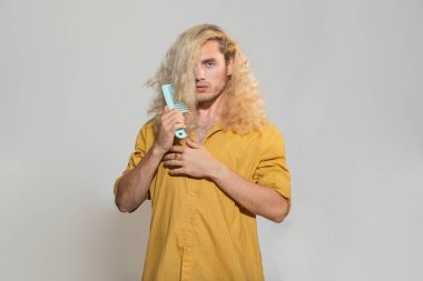 Saçlarını tarayan yakışıklı bir adamın portresi. Saç modelini kapat, erkek fırçası saç modelini al, gri arka plan ayır. Saç fırçalayan adam.