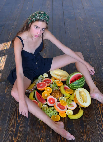 Vacker ung flicka sitter på ett golv med sommarfrukter. — Stockfoto