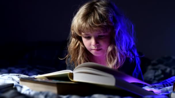 Un chico lindo leyendo un libro acostado en la cama. Concepto de educación y lectura. El desarrollo infantil de la fantasía. — Vídeo de stock
