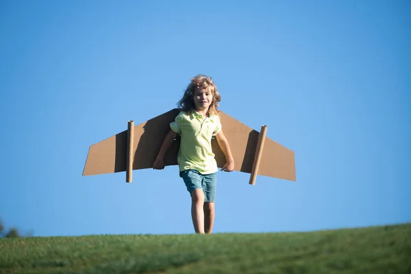 I bambini volano. Divertente bambino pilota ragazzo che vola con ali di cartone giocattolo aeroplano sul cielo blu, spazio copia. Avviare il concetto di libertà, bambino spensierato. — Foto Stock