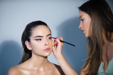 Makyöz göz farı sürüyor. Vizeci bir el, genç bir güzellik modelinin kozmetik ürünlerini boyuyor. Moda cilt üzerinde parlak fosforlu kalem. Profesyonel makyaj süreci.