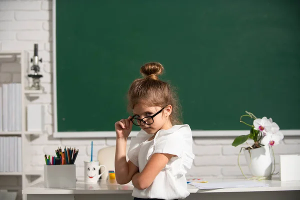 Głupia uczennica w okularach na tablicy. Cute little school girl nauka w klasie. — Zdjęcie stockowe