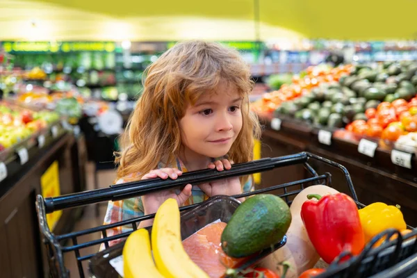 Un bambino al supermercato. Carino piccolo ragazzo arguzia carrello della spesa scegliendo merci al negozio di alimentari o supermercato. Ragazzo divertendosi mentre sceglie il cibo al supermercato. — Foto Stock