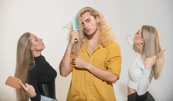 Piękna młoda para kobiet z długimi błyszczącymi jedwabistymi włosami i mężczyzna z blond kręconymi włosami grzebie włosy grzebieniem. Portret grupowy młodych ludzi czesających włosy. — Zdjęcie stockowe