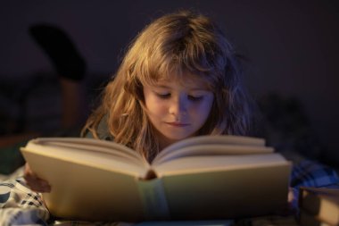 Kitap okuyan şirin bir çocuk. Açık kitabı olan bir çocuk. Ev okulu dersi. Evde kitap okumaya odaklanmış küçük bir çocuk. Çocukların hayal gücünün gelişimi..