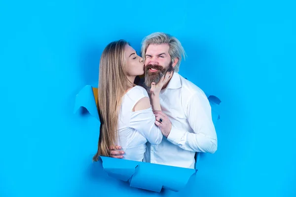 Paar gaten in blauw papier, kopieer ruimte voor tekst of slogan. Korting en verkoop, mensen met een achtergrond. Verrast paar van bebaarde man en gelukkige vrouw maken gat in papier kijken door gat. — Stockfoto