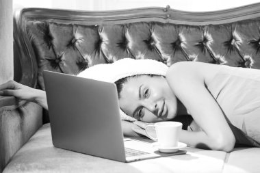 Kahve ve dizüstü bilgisayarı olan ve lüks yatak odasındaki rahat bir kanepede dinlenen bir kız. Çekici seksi kadın otel odasında bornoz ve havlu giyerek rahatlıyor..