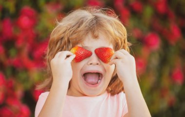 Çilekle çocuk eğlencesi. Yazın açık havada çilek tutan neşeli çocuk..
