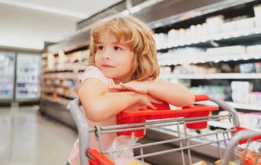Marketten alışveriş sepeti alan bir çocuk. Müşteri çocuk süpermarketten ürün satın alıyor.