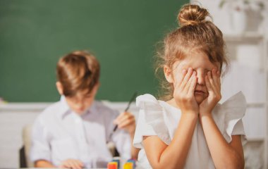 Zeki bir liseli kız ağlar. Okul üniformalı kız koluyla yüzünü örterek okulda karatahtanın önünde zorbalığa uğradığı için üzülüyor. Çocukluk ve eğitim sorunları kavramı.