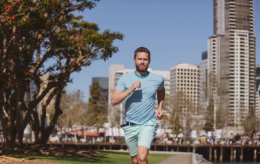 Erkek koşucu güzel bir yaz gününde şehirde koşuyor..