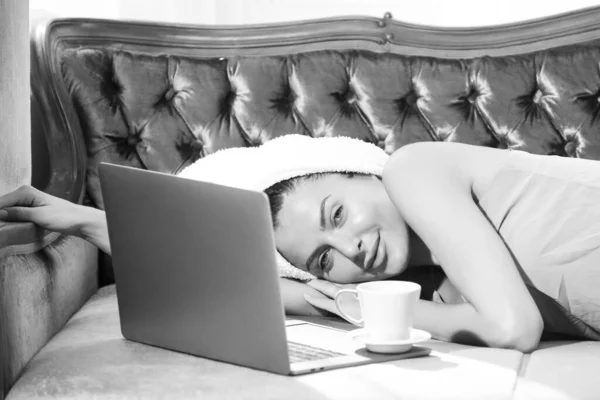 Ragazza con caffè e laptop a riposo e posa in accogliente divano letto nella camera da letto di lusso una mattina facile. Attraente donna sexy rilassante indossando accappatoi e asciugamani in camera d'albergo. — Foto Stock