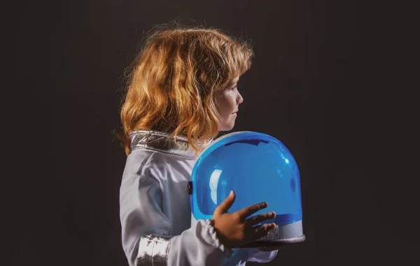 Ritratto di bambino divertente con casco da astronauta. Carino bambino astronauta ragazzo in tuta spaziale che tiene il casco su sfondo nero. — Foto Stock