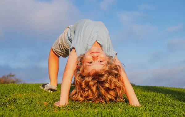 Mutlu kız çocuğu yaz günü çimlerin üzerinde baş aşağı duruyor. Egzersiz yapan sevimli çocuk..