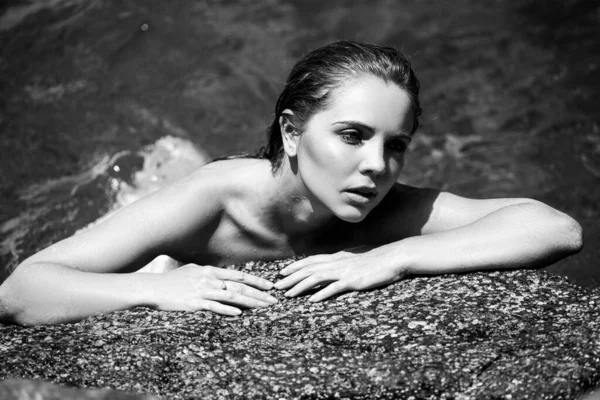 Bella giovane donna che si rilassa sulla spiaggia al tramonto seduta su una roccia. Donna alla moda in posa su una spiaggia con rocce. — Foto Stock