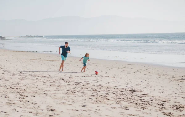 父と息子はビーチでサッカーやサッカーをします。夏の日に子供の男の子とパパ. — ストック写真