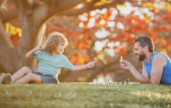 Father and child son playing chess lying on grass at lawn park. Fathers Day, love family, parenthood, childhood concept. — Stock Photo, Image