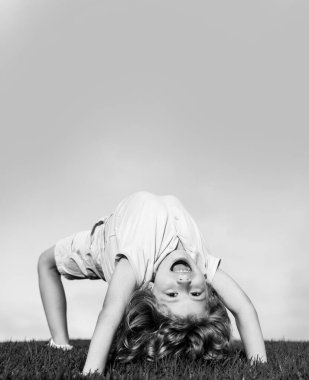 Yeşil çimlerin üzerinde baş aşağı duran mutlu çocuk. Gülen çocuk bahar parkında eğleniyor. Sağlıklı çocuk yaşam tarzı konsepti. Spor çocuğu egzersiz yapıyor. İfade ifadesi.