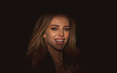 Çekici ve şehvetli görünen güzel gülümseyen kadın modelinin portresi. Siyaha izole edilmiş dramatik stüdyo ışığı olan güzel bir yüz. Karanlıkta güzel bir kadın yüzü. Şehvetli gülümseme, gülen yüz.