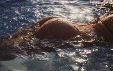 Sexy buttocks in pool closeup, summer journey, sensual woman with hot natural butt relax in water. Wet body, ass in sexy bikini. Seduction and pleasure model. Luxury passion buttocks.
