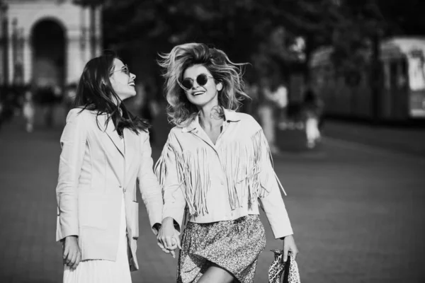 两个兴奋的女人在街上走着漂亮的女孩在城市里散步时与朋友牵着手。两个笑着的姐妹在户外合影. — 图库照片
