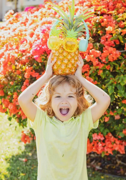 Garoto engraçado criança com um abacaxi na cabeça no parque de verão verde. — Fotografia de Stock