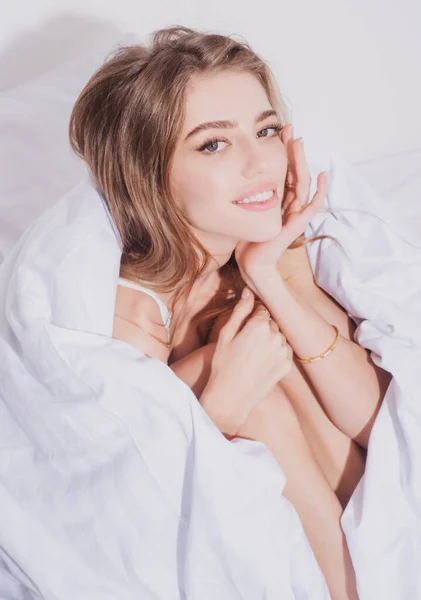 Mujer sensual envuelta en una suave manta sentada en la cama. Mujer sexy sentada en la cama y sonriendo en casa. — Foto de Stock