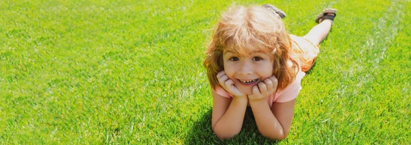 Banner with spring child face. Kids laying in grass, cute child in summer nature park. Kids on green grass background. — Stock Photo, Image