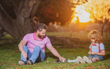 Baba oğluyla satranç oynar. Aktif insanlar parkta satranç oynayıp eğleniyorlar. Çocukla vakit geçiriyorlar. Aile dışı oyun.