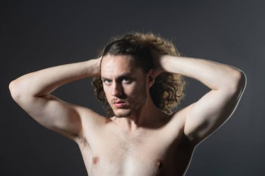 Çıplak gövdeli ve kıvırcık saçlı bir adam. Gri arka plan fotokopi alanında izole edilmiş mükemmel kıvırcık saçlı çekici, kaslı esmer adamın yakın portresi..