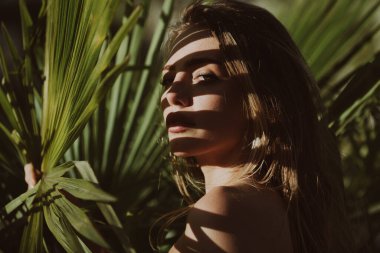 Genç kadınlar tropikal yapraklarla yüzyüze gelirler. Doğal çıplak makyajlı, mükemmel ciltli, sarı saçlı bir kadının yakın plan portresi. Doğal kozmetik, sağlık, cilt bakımı ve güzellik..