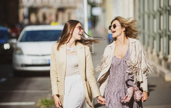 Dos jóvenes lanzadoras con gafas de sol caminando por la ciudad. Vacaciones divertidas, viajes románticos. —  Fotos de Stock