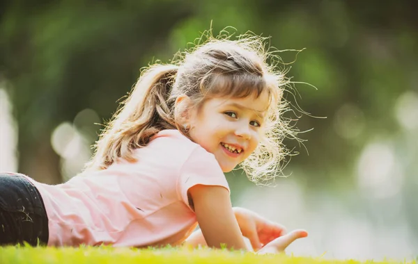 Glad flicka avkopplande och liggande på våren eller sommaren gräs utomhus. Söta barn ligger på park gräsmatta. — Stockfoto