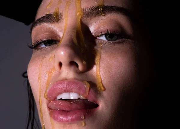 Portret van een jonge vrouw. Mooie meisjes tong likken honinglippen. Sensuele jonge vrouw gezicht met honing druppel van dichtbij. Sexy model met honing drup op gezicht. — Stockfoto