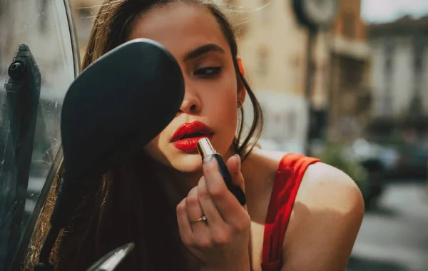 Mode flicka med röda läppar sätta läppstift tittar i en bakre. Gatumodell. Stadslivet. Makeup i rörelse. — Stockfoto