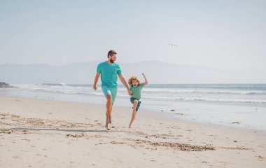 Baba oğul sahilde koşuyor. Baba ve çocuk dışarıda oynuyorlar. Mutlu aile kavramı.