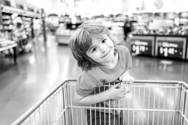 Funny customer boy child holdind trolley, shopping at supermarket, grocery store.