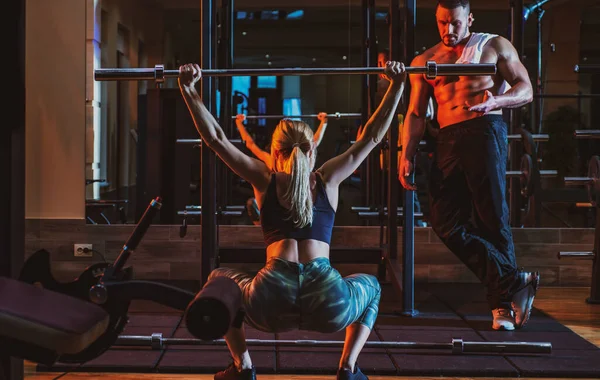 Mujer entrenando con barra en el gimnasio. Entrenador muscular hombre mujer de entrenamiento con barra. Instructor de fitness entrenador personal. — Foto de Stock