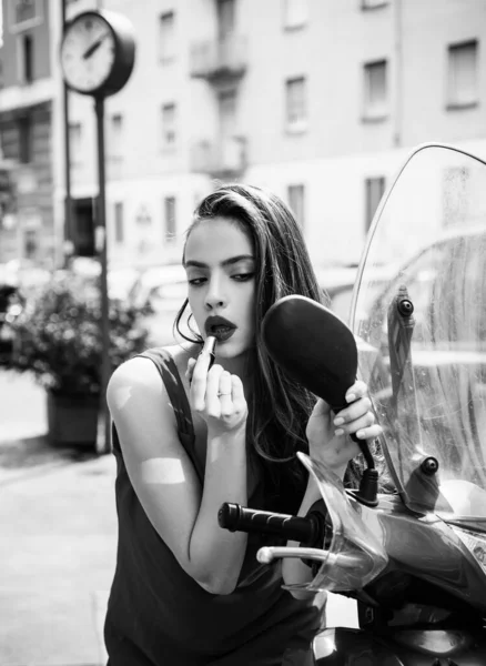 Нанесення макіяжу на вулицю. Сексуальна дівчина моди з червоними губами поклала помаду, дивлячись у дзеркало мотоцикла . — стокове фото