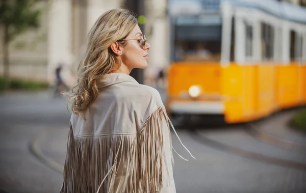 Foto de rua estilo de mulher elegante moda vestindo roupas da moda. Modelo andando na rua da cidade europeia no fundo do ônibus trolleybus. — Fotografia de Stock
