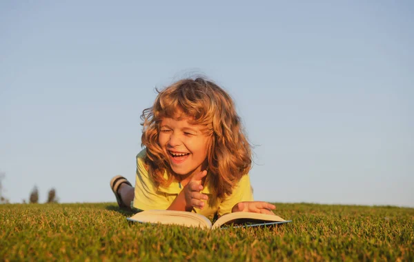 Niño lectura libro que pone en la hierba sobre la hierba y el fondo del cielo con espacio de copia al aire libre. — Foto de Stock